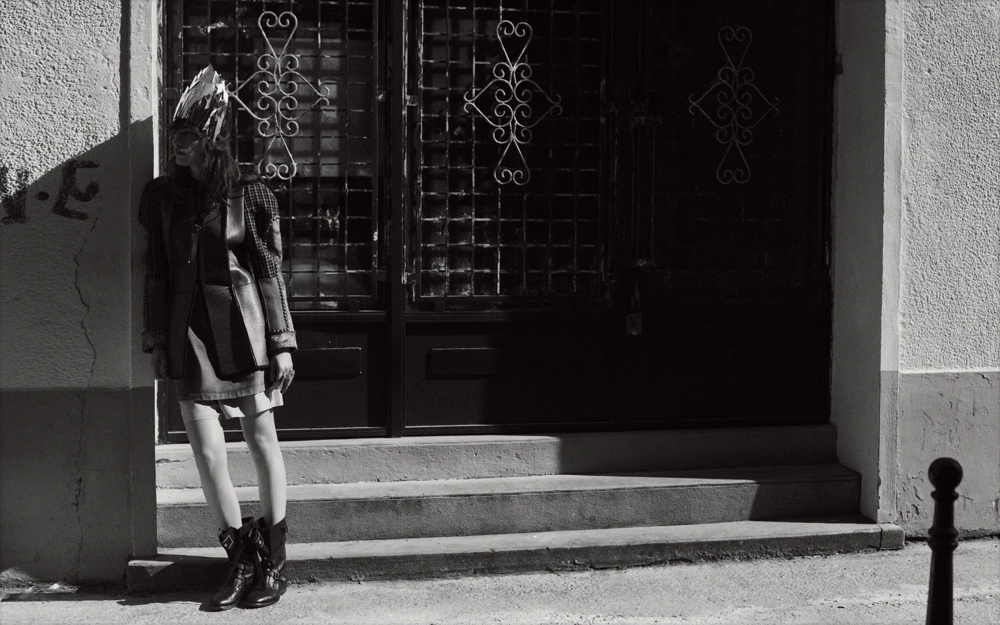 Monochrome fashion portrait of a model wearing an ornate crown and dark boots leaning against an entryway by Eminente Creative Production