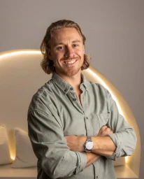Portrait of a smiling man with arms crossed wearing a sage green button-down shirt and a silver wristwatch.