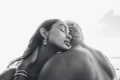 Close-up black and white portrait of a woman with her eyes closed, embracing a person while wearing dangling earrings and bracelets.