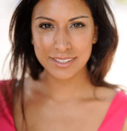 Close-up portrait of a smiling woman with long brown hair wearing a bright pink top against a neutral background.