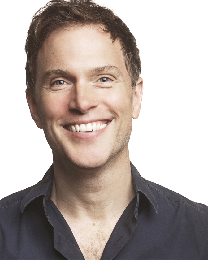 Headshot of a smiling adult male with fair skin and brown hair, wearing a dark blue button-down shirt, against a white background in a photo studio.