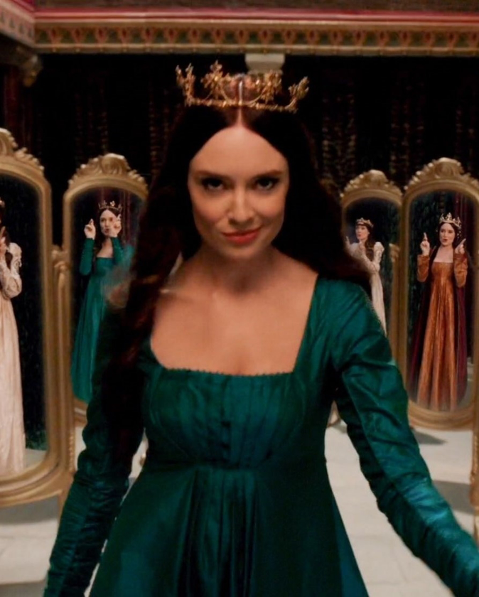 Woman in a green dress and gold crown is reflected in multiple mirrors indoors, creating a regal and elegant scene with rich colors.