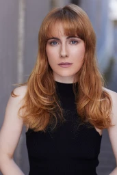 Portrait of a woman with red hair and bangs wearing a black sleeveless top against an urban outdoor wall in Sydney