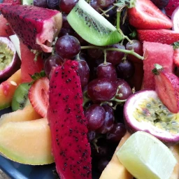 Assorted fresh tropical and summer fruits including dragon fruit, grapes, kiwi, strawberries, passion fruit, and melon.