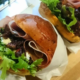 Two gourmet sandwiches filled with cured meat, lettuce, and cheese wrapped in paper