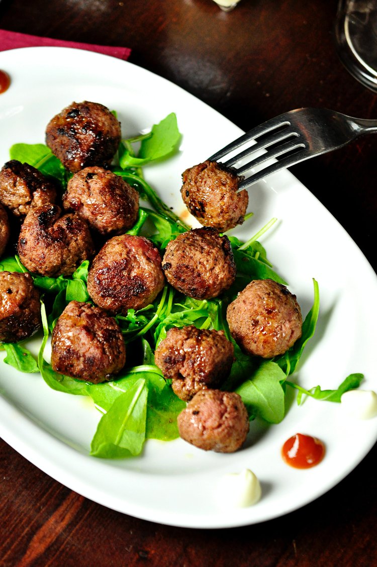 Overhead shot of meatballs on a white plate with green arugula, accompanied by a fork poised to pick up one of the meatballs.
