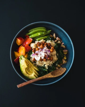 Overhead shot of a dark bowl filled with quinoa, vegetables, and avocado against a dark background. Healthy eating concept.