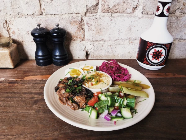 Overhead shot of assorted Middle Eastern food plate with hummus, hard-boiled eggs, vegetables, and condiments on a wood table.