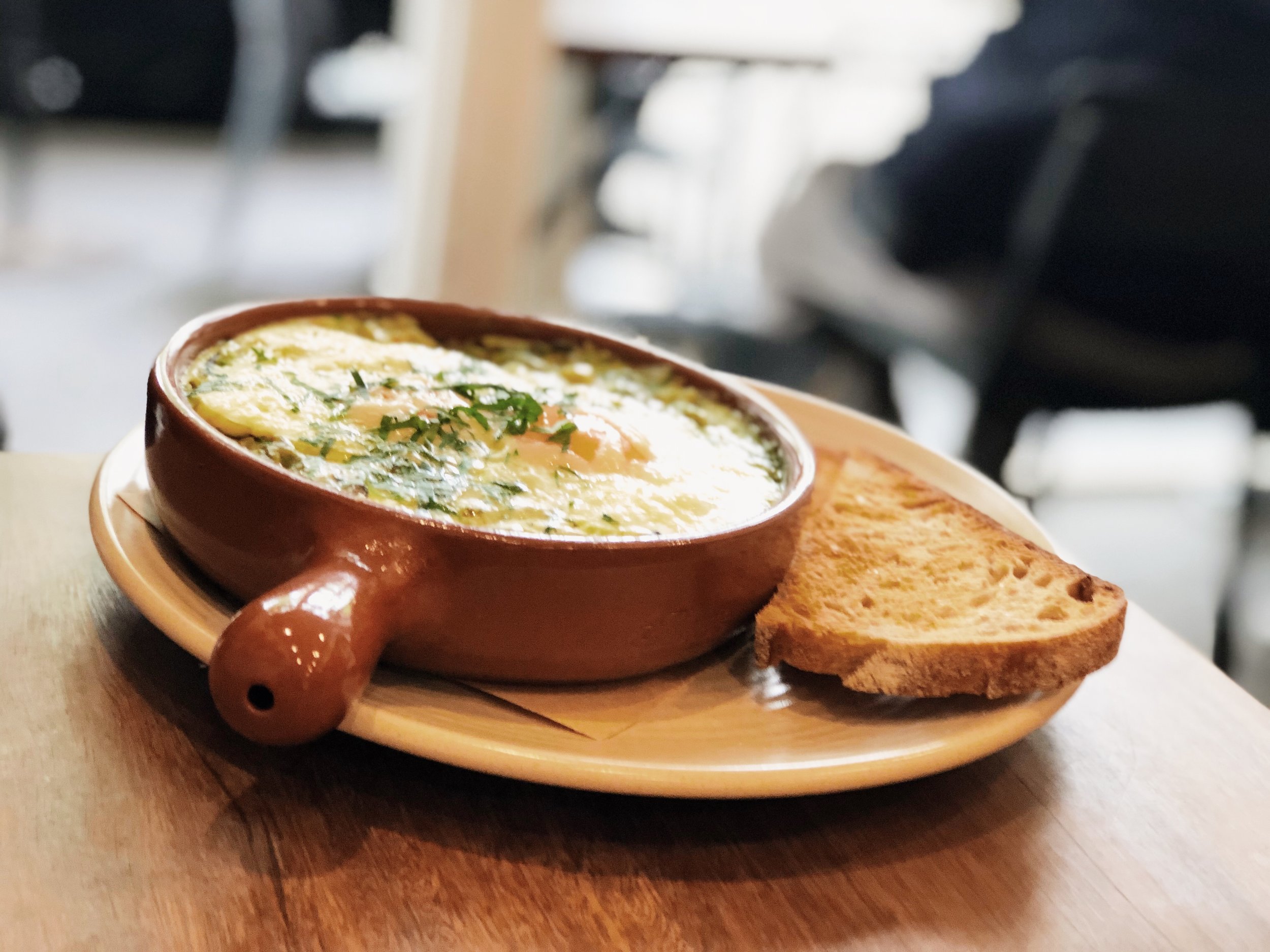 Baked egg dish in a ramekin served with toast on a wooden table in a restaurant, capturing a cozy and delicious meal.