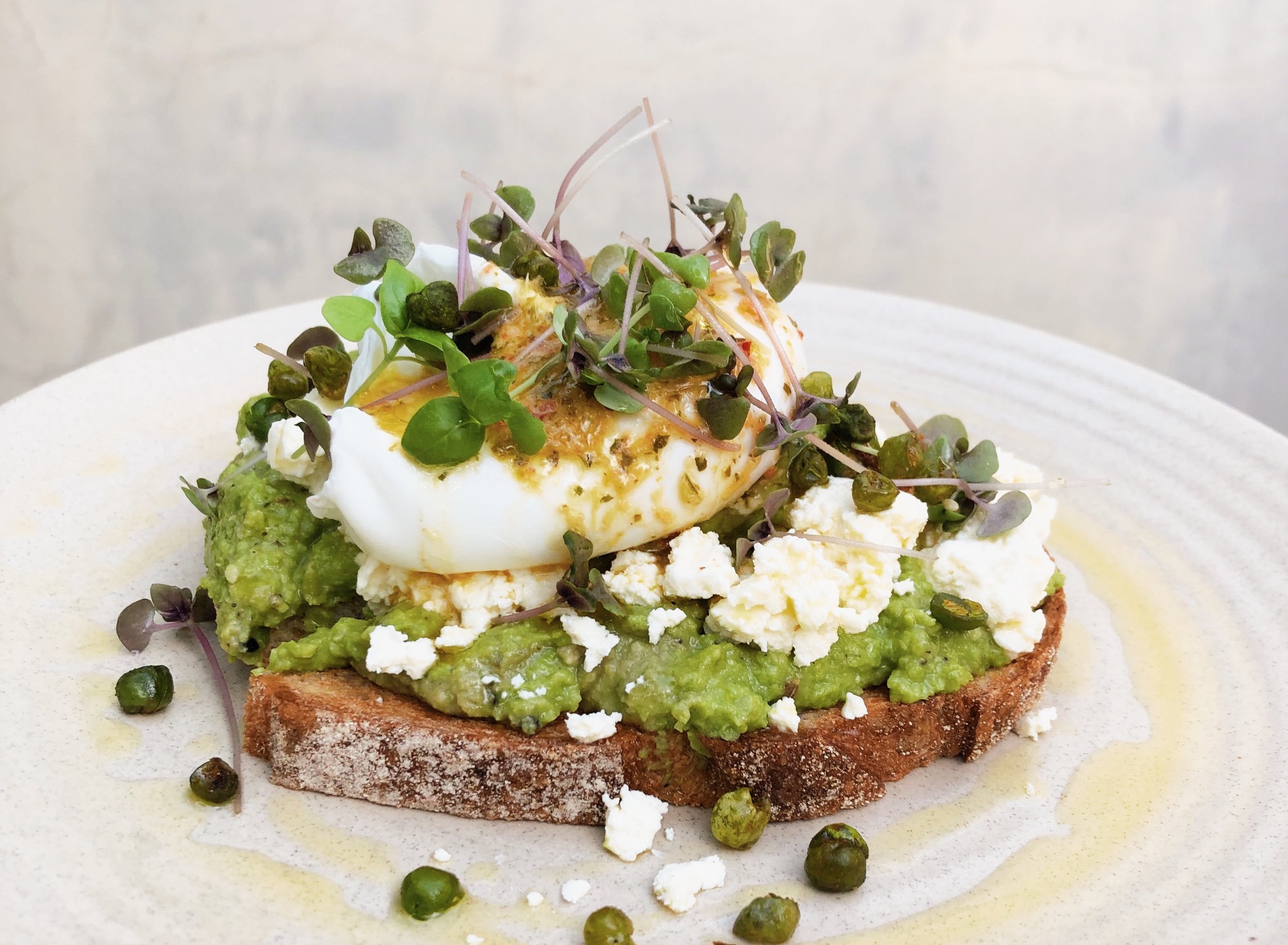 Overhead shot of avocado toast topped with a poached egg, feta cheese, and microgreens, served on a white plate.
