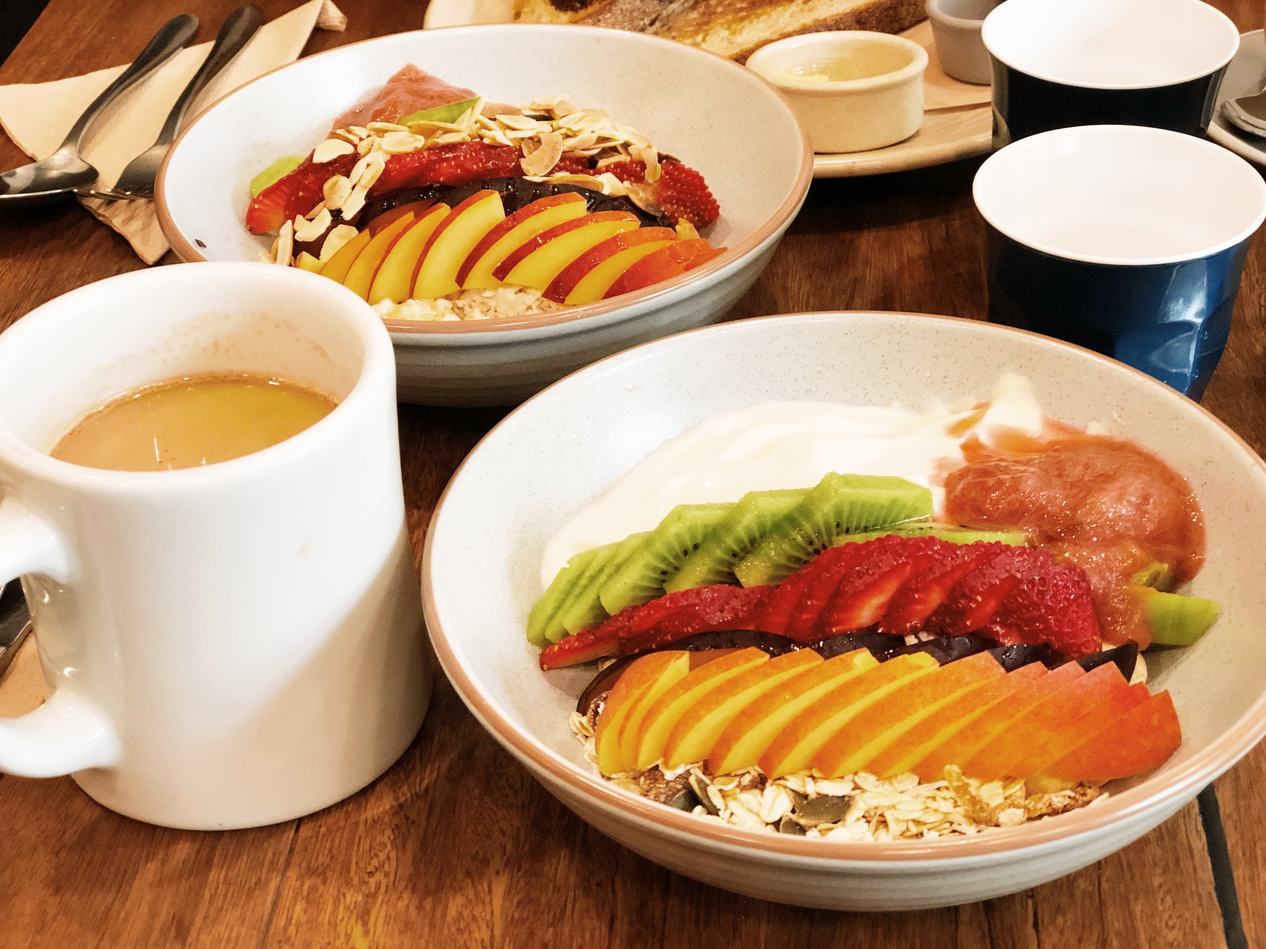 Overhead shot of two bowls with a base of granola topped with yogurt and fresh fruit like kiwi, strawberries, and peaches.
