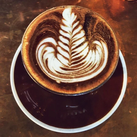 Top-down view of a ceramic cup of coffee with detailed leaf pattern latte art on a saucer in Sydney