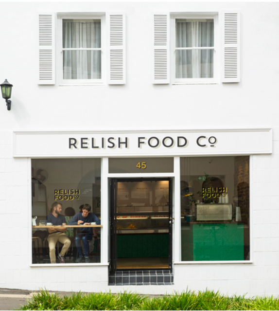 Exterior of Relish Food Co. restaurant with two people visible through the window, white building facade, and black signage.