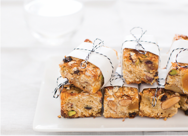 Stack of granola bars wrapped in white paper and tied with twine, placed on a white plate against a blurred white background.