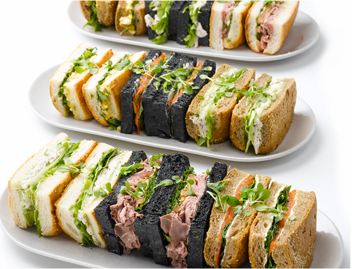 Three plates of assorted sandwiches featuring different breads and fillings, with fresh greens, on a plain white background.