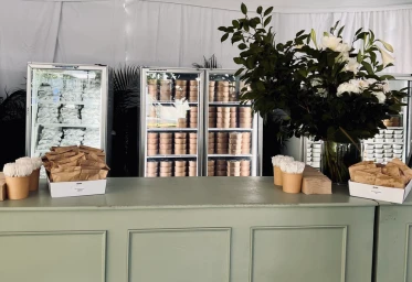 Catering setup by Relish Food & Co in Sydney featuring a green counter, stocked display refrigerators, and floral arrangement.
