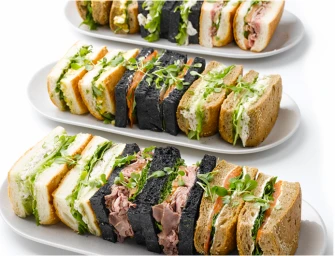 Assorted gourmet sandwiches on three oval white platters against a clean white background by Relish Food & Co in Sydney
