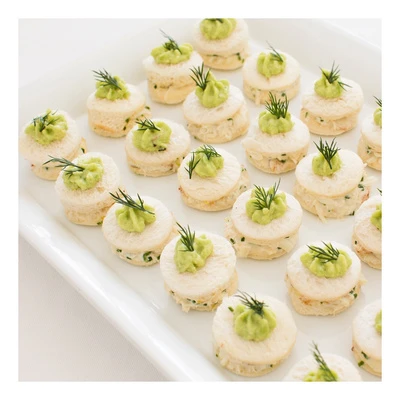 Round canape sandwiches topped with green puree and fresh dill on a white platter