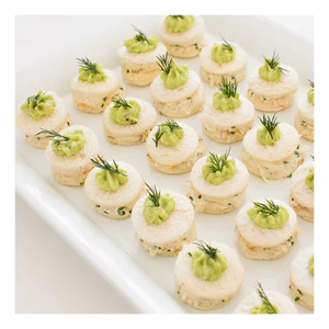 Round canape sandwiches topped with green puree and fresh dill on a white platter