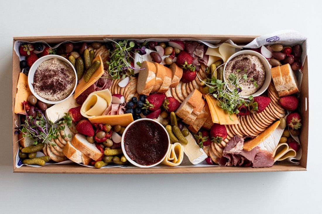 Overhead shot of a catering tray filled with an assortment of cheeses, fruits, breads, crackers, pickles, dips, and cold cuts.