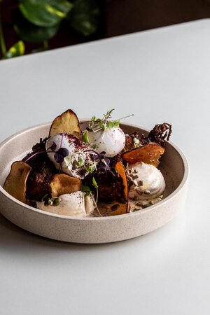 Close-up of a culinary creation in a beige bowl: roasted potatoes, poached eggs, cream sauce, and garnished with herbs.