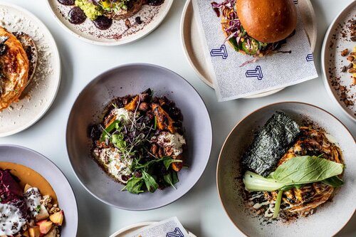 Overhead shot of an assortment of beautifully plated dishes on a white surface, showcasing gourmet food presentation and culinary artistry.