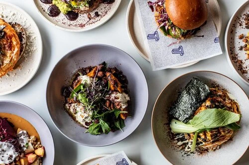 Overhead shot of an assortment of beautifully plated dishes on a white surface, showcasing gourmet food presentation and culinary artistry.