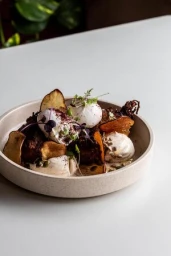 Plated gourmet dish with poached eggs, vegetable crisps, and herbs in a ceramic bowl on a white table.