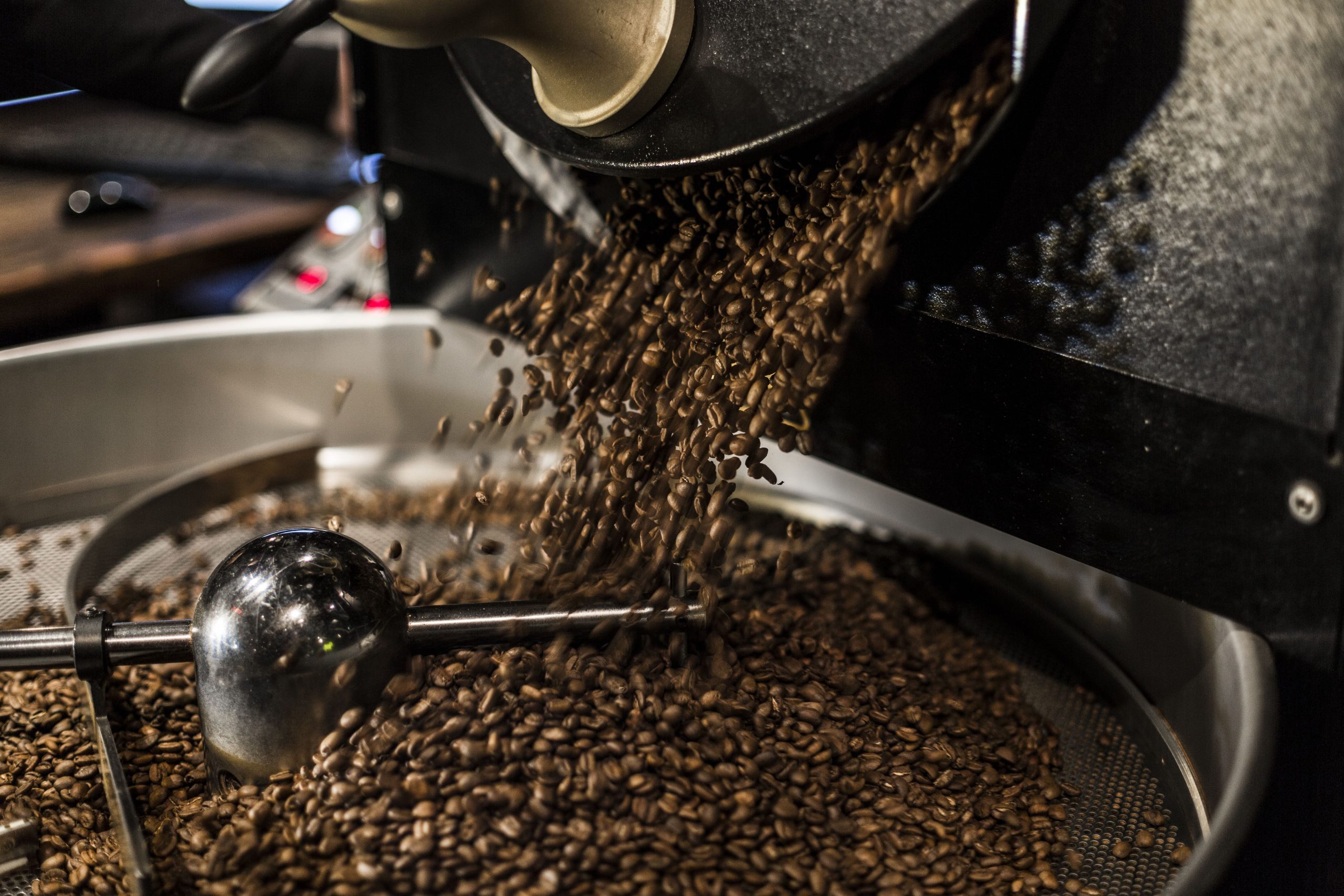 Coffee beans cascading from a roasting machine into a metal cooling tray, industrial and rich, brown color palette