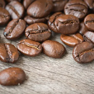 Macro shot of coffee beans on a wooden surface showcasing their rich color, texture, and organic forms. Food and beverage.