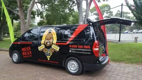 Black mobile coffee van parked on a brick path with open rear door and green and red flags outdoors in Sydney