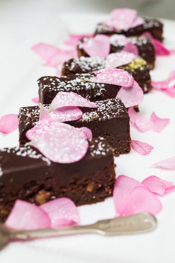 Arrangement of chocolate brownie squares, garnished with powdered sugar and pink flower petals, served on a white platter.