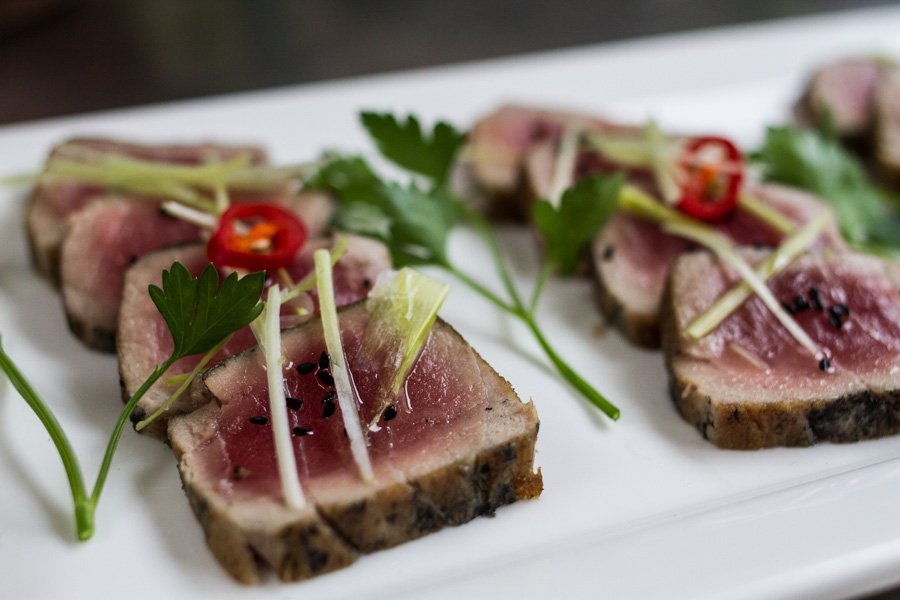 Seared tuna slices are arranged on a white plate, garnished with cilantro and peppers, showcasing a close-up of the culinary dish.