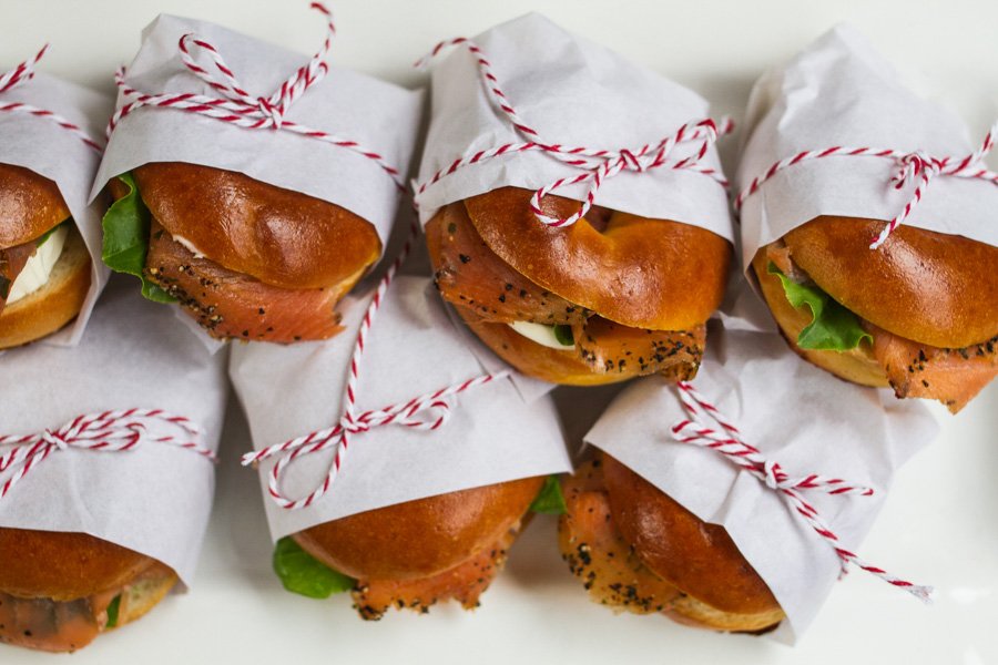 Bagel sandwiches wrapped in white paper and tied with red and white string, perfect for a picnic or lunch spread.