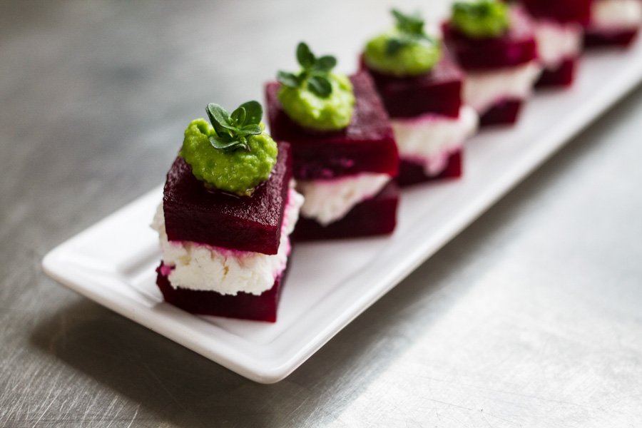 Elevated view of beet and cheese appetizers arranged on a white rectangular plate, topped with green garnish on a metallic surface.