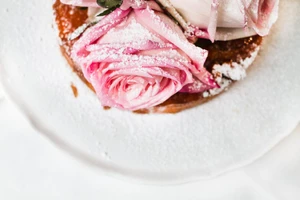 Close up of a dessert tart topped with fresh pink roses and a dusting of powdered sugar on a white plate.