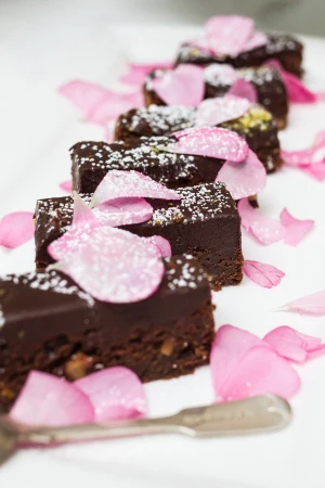 A line of chocolate brownies decorated with powdered sugar and pink flower petals on a white platter.