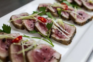 Seared tuna slices garnished with herbs and red chili on a white platter by Urban Cooking Collective in Sydney.