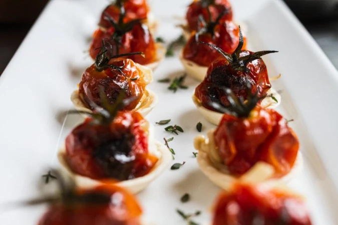 Close-up of roasted cherry tomato tarts garnished with herbs on a long white serving platter by Urban Cooking Collective