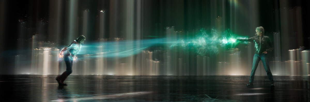 Two adults, one running from a beam of green energy projected by the other, with blurred figures and an indistinct interior location.