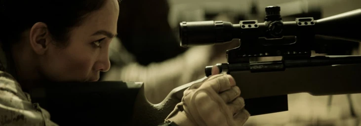 Close-up profile of a woman aiming a sniper rifle with a mounted scope, wearing fingerless tactical gloves.