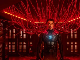 Man in futuristic armored suit standing beneath an intricate web of glowing red cables inside a server room