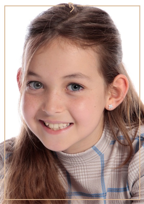 Close-up portrait of a smiling preteen girl with long hair and a plaid shirt in a studio setting, highlighting her clear complexion.