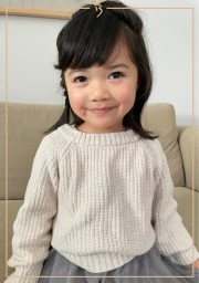 Young child wearing a cream knit sweater and grey tulle skirt sitting on a sofa, by Bettina Childrens.