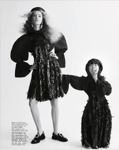 Fashion editorial shot of an adult and child model wearing matching black dresses with fringe and cap accessories against a white backdrop.