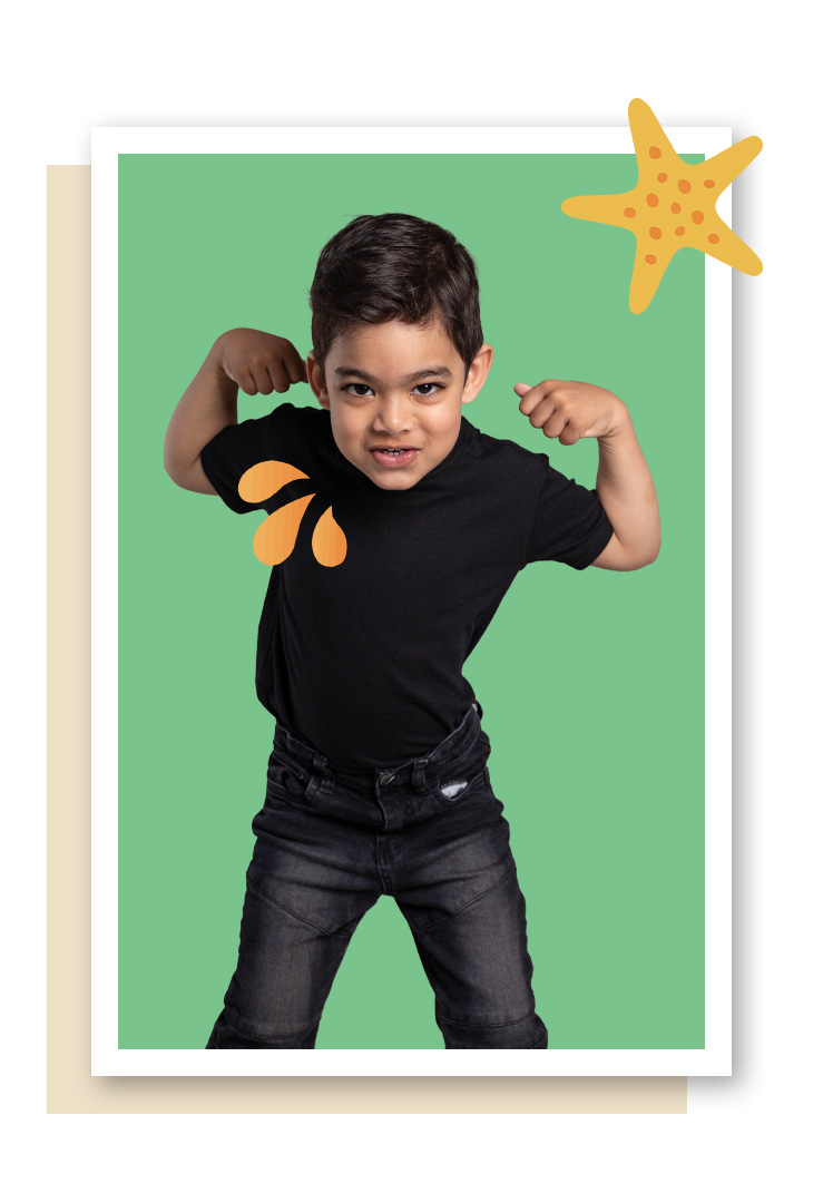 A young boy flexing his biceps in front of a green background with a starfish sticker and orange paper shapes on his shirt.