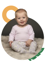 Baby wearing a pink top and patterned leggings sitting on a fluffy blanket in a studio portrait by Bubblegum Casting