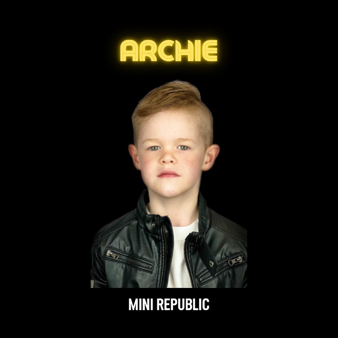 Portrait of a young boy with blond hair wearing a black jacket against a black background. The text "Archie" is at the top.