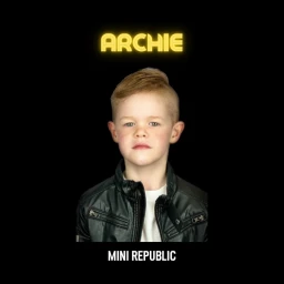 Portrait of a young boy with reddish-brown hair wearing a black leather jacket against a black background with yellow neon name text above.