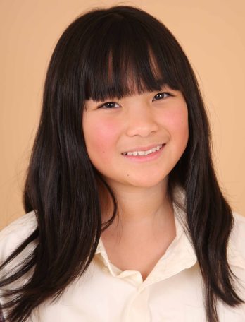 Portrait of a young Asian child with black hair and a collared shirt, captured in a photo studio with even lighting.